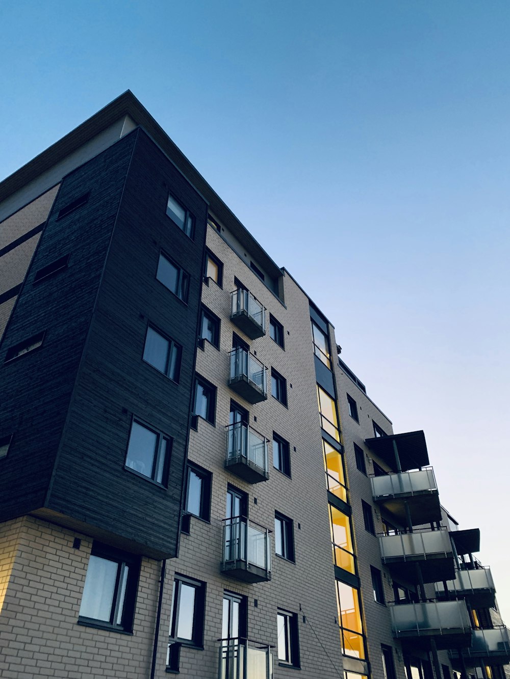 Edificio de viviendas en ladrillo gris y madera oscura con balcones, recortado contra el cielo del atardecer