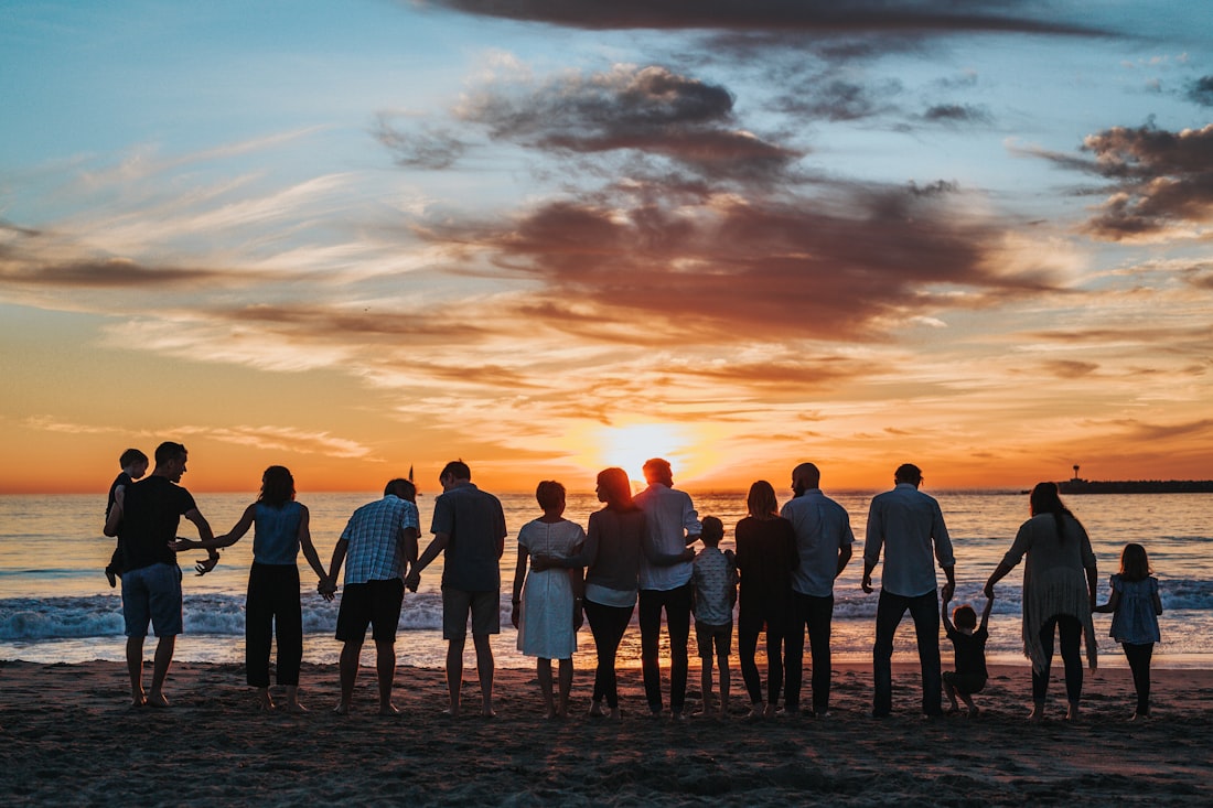 Familia de varias generaciones tomada de la mano frente al mar al atardecer